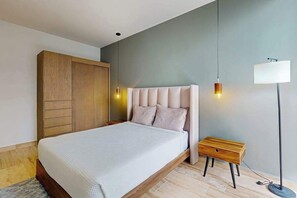A bedroom with a bed, bedside table, lamp, wardrobe, and a hanging light fixture. - Modern 1BR Condo | Rooftop Pool & Gym, Near Beach (Playa del Carmen)