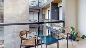 A multi-level interior with wicker chairs and a glass table, a potted plant, and a view through a glass railing. - Modern 1BR Condo | Rooftop Pool & Gym, Near Beach (Playa del Carmen)
