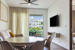 A modern hotel room with a dining area, a ceiling fan, a TV mounted on the wall, and a balcony with a view of the surrounding buildings. - Playacar Resort Condo - 3 Pools & Gym - Sleeps 6 (Playa del Carmen)