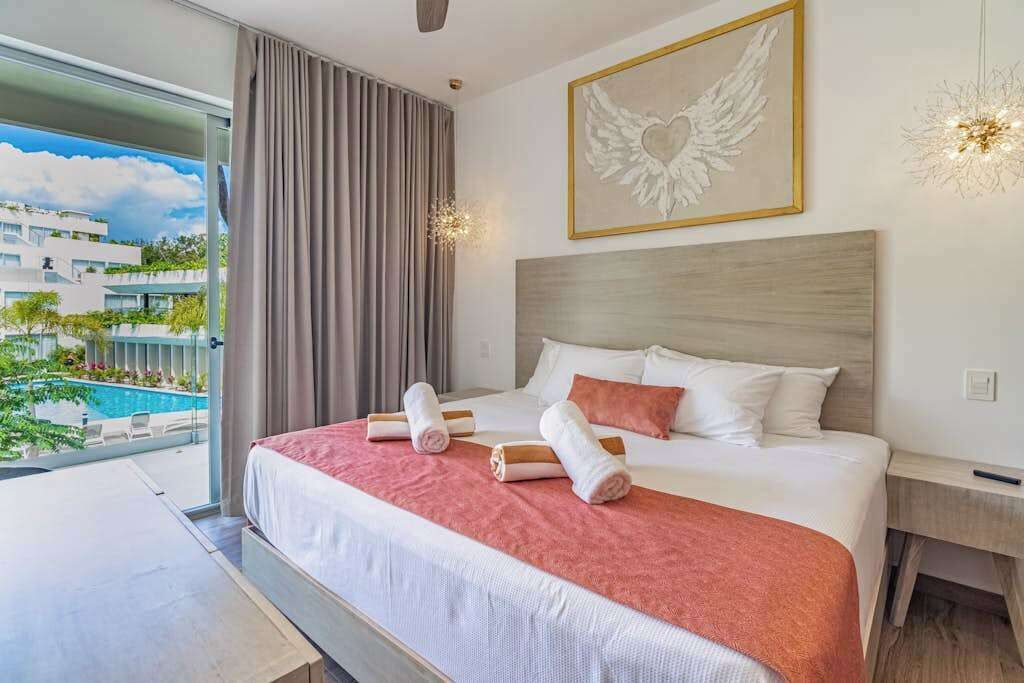 Een hotelkamer met een groot bed, uitzicht op een zwembad en een schilderij van een engel aan de muur.