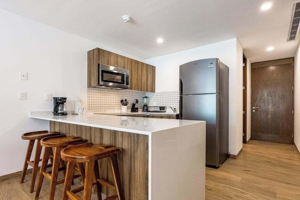 A modern kitchen with a central island, bar stools, a microwave, a refrigerator, and wooden cabinets.