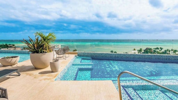 Une piscine à l’eau d’un bleu cristallin, un palmier et une vue sur l’océan.