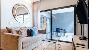 Un salon moderne avec un canapé, une table basse, un téléviseur et un balcon équipé de chaises.