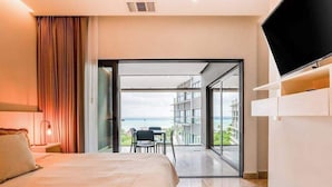 Une chambre d’hôtel comprenant un lit, une télévision, un balcon avec vue sur la mer et un coin repas.