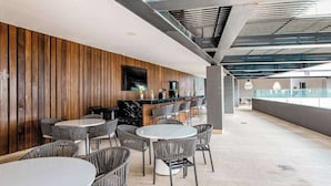 Un intérieur moderne avec un mur lambrissé en bois, un espace bar avec des sièges et un plafond haut avec des poutres apparentes.