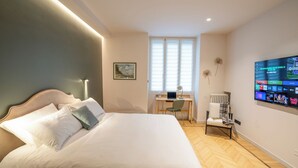 Ein Schlafzimmer mit Bett, Schreibtisch, Stuhl, Heizkörper und einem an der Wand befestigten Fernseher.
