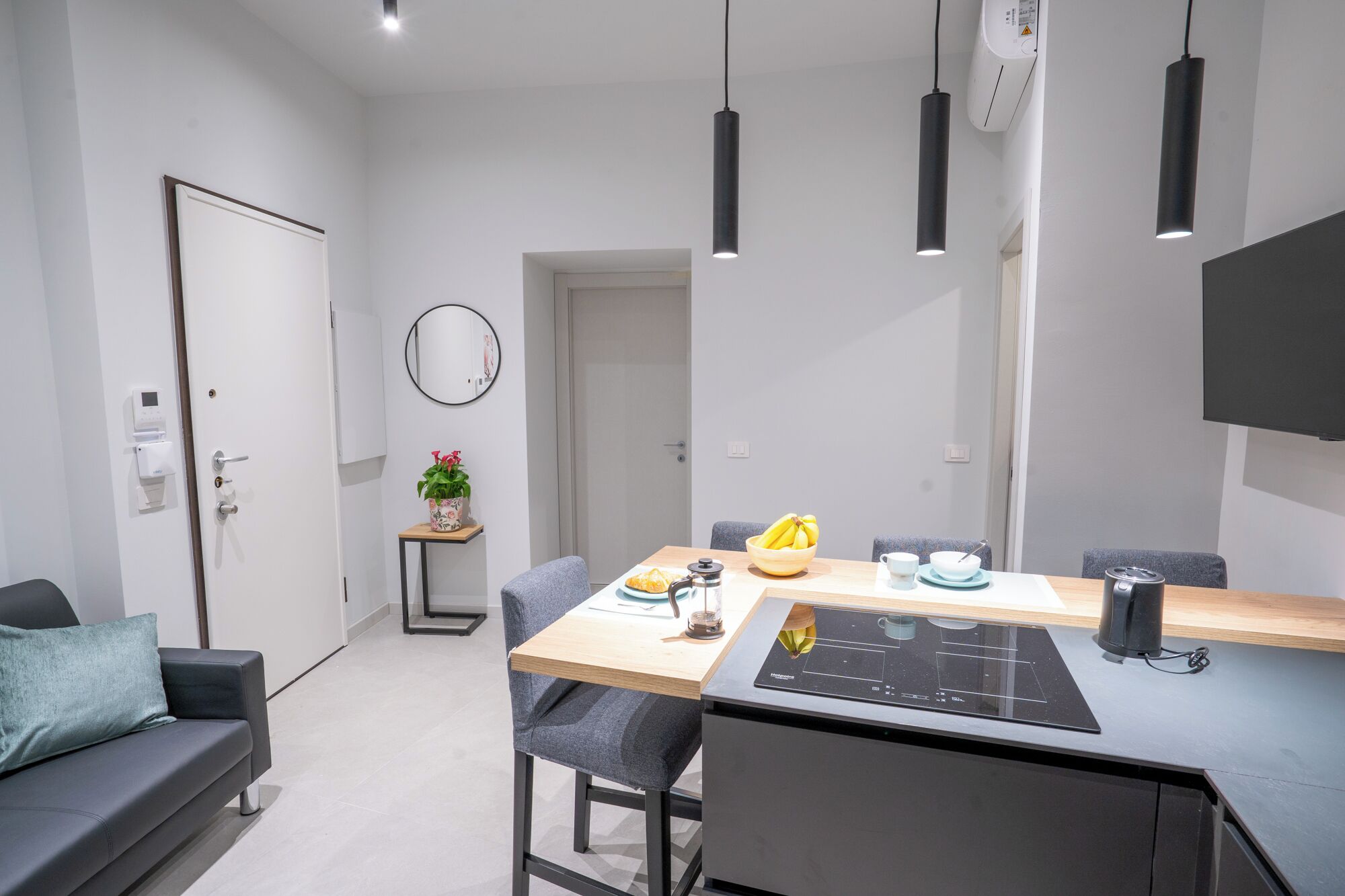 Una cocina moderna con una placa de inducción empotrada, una mesa de comedor con sillas, una planta pequeña en maceta y un espejo fijado a la pared.