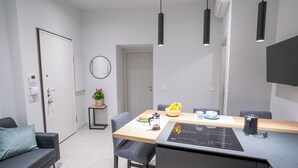 Eine moderne Küche mit integriertem Induktionskochfeld, einem Esstisch mit Stühlen, einem kleinen Topfpflanzen und einem an der Wand befestigten Spiegel.