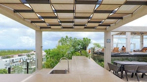 An outdoor kitchen area with a sink and seating, overlooking a residential area and greenery. - Playa Studio | Rooftop Pool & Balcony (Playa del Carmen)