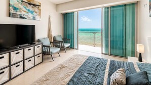Une chambre avec une télévision, un lit, un bureau, une chaise et une vue sur la plage.