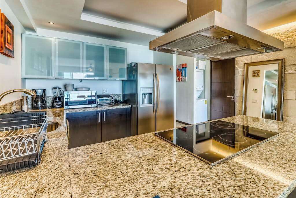 Une cuisine moderne dotée de plans de travail en granit, d’appareils électroménagers en acier inoxydable et d’un îlot central.