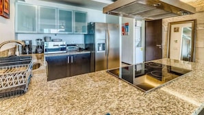 Une cuisine moderne dotée de plans de travail en granit, d’appareils électroménagers en acier inoxydable et d’un îlot central.