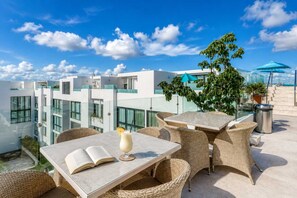 A rooftop terrace with outdoor seating, a view of modern buildings, and a clear sky. - Modern Playa del Carmen Apt: Rooftop Pool & WiFi (Playa del Carmen)