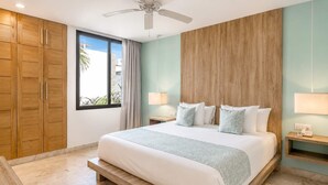 Une chambre dotée d’un grand lit, d’une armoire en bois, d’un ventilateur de plafond et offrant une vue sur l’extérieur.
