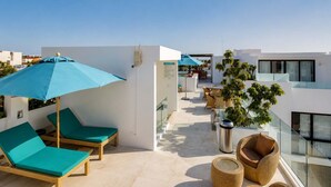 Une terrasse sur le toit, avec des chaises longues, un parasol bleu, des meubles en osier et une vue sur la ville.