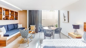Een moderne hotelkamer met een bank, eettafel, stoelen, een bed en een boekenkast.