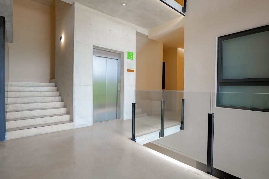 Un intérieur moderne avec un escalier, un ascenseur et une rambarde en verre.