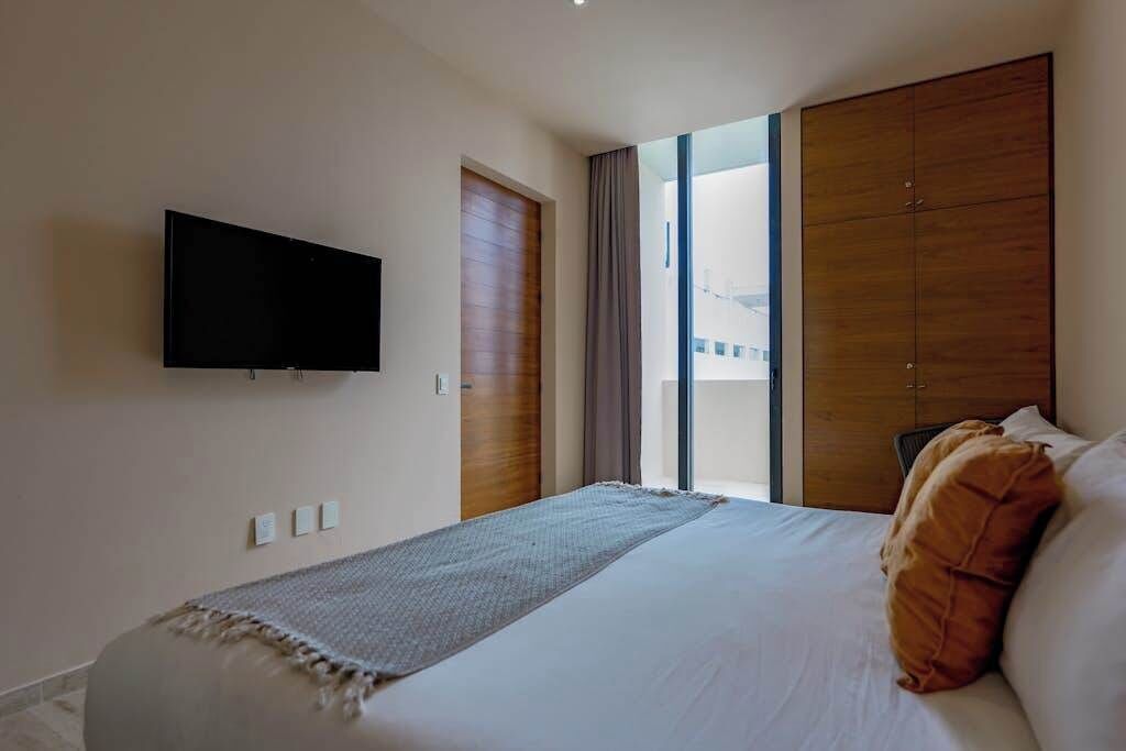 A hotel room with a bed, a television mounted on the wall, a window with curtains, and a wardrobe.