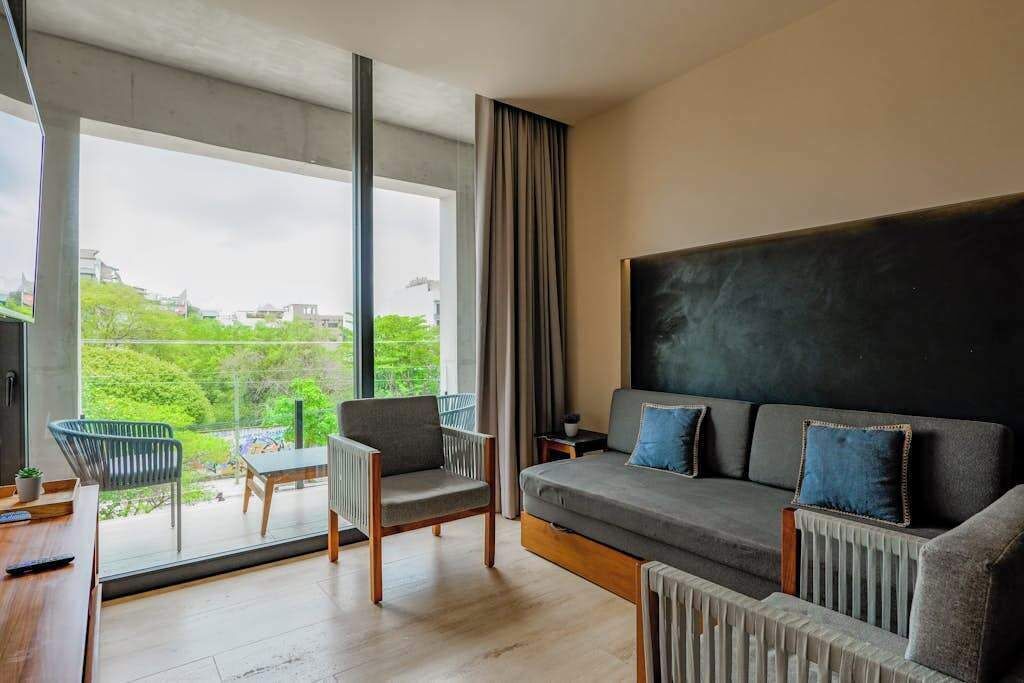 Una sala de estar moderna con un sofá, sillas, una mesa y un amplio ventanal con vista a la ciudad.