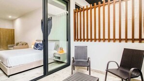 Una camera d'albergo con un letto, un tavolino, due sedie e una porta-vetro scorrevole che dà su un balcone con una ringhiera in legno.