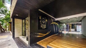 Esterno di un edificio moderno con un'insegna nera e dorata, una panchina in legno e un ingresso in vetro.
