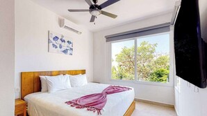A bedroom with a bed, a ceiling fan, a window with a view, and a flat-screen TV. - 1BR condo near Akumal beach, rooftop pool (Akumal)