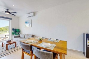 A dining area with a wooden table set for four, a sofa, a ceiling fan, and a refrigerator. - 1BR condo near Akumal beach, rooftop pool (Akumal)