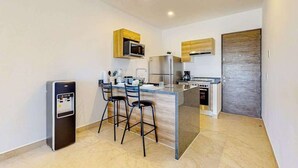 A compact kitchen with a refrigerator, microwave, and stove, a water dispenser, and a bar area with stools. - 1BR condo near Akumal beach, rooftop pool (Akumal)