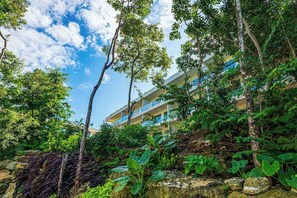 A hotel with multiple floors, surrounded by lush greenery and trees. - Playacar 1BR Condo | Pools, Balcony & WiFi (Playa del Carmen)