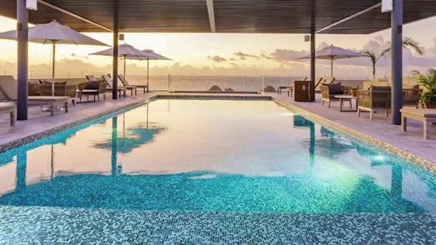 A pool with lounge chairs and umbrellas, a covered area, and a view of the ocean. - Oceanfront 2BR, Rooftop Pool, Gym, Walk to Beach (Playa del Carmen)