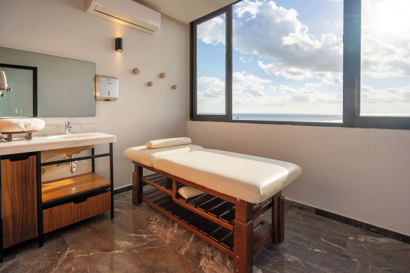 Une salle de bain moderne avec une grande fenêtre, un banc en bois, une coiffeuse avec un miroir et un lavabo.