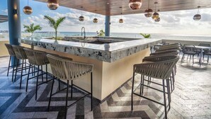 A bar area with a marble countertop, bar stools, and hanging pendant lights. - Oceanfront 2BR, Rooftop Pool, Gym, Walk to Beach (Playa del Carmen)