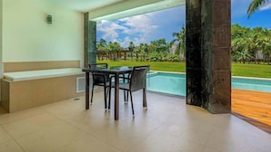 A room with a pool, a table with chairs, and a view of a garden. - Beachfront 3BR Condo, Resort Pool | Playa (Playa del Carmen)