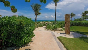 A pathway leading to a beach with palm trees and a stone structure. - Beachfront 3BR Condo, Resort Pool | Playa (Playa del Carmen)