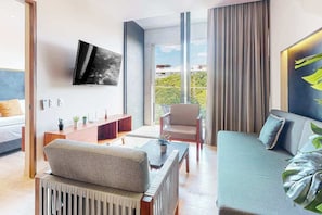 A modern hotel room with a sofa, armchair, and a TV mounted on the wall. - Playa del Carmen Condo | Rooftop Pool & Balcony (Playa del Carmen)