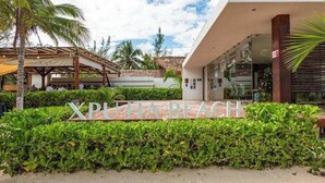 Un cartel con la inscripción 'XPULAHABEACH', un edificio moderno y una zona cubierta con palmeras.