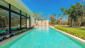 Una piscina moderna con agua cristalina, rodeada de un césped cuidado y árboles.