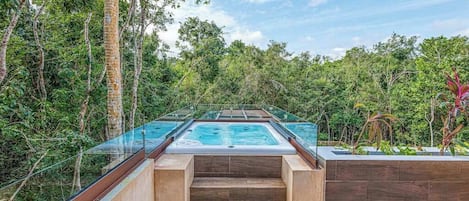 A glass-enclosed hot tub with steps leading down to a pool, surrounded by dense forest.
