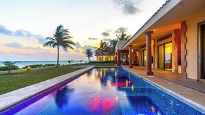 A swimming pool with a view of the ocean and palm trees, a covered area with columns, and a building with a red roof. - Beachfront 5BR Villa Playacar, Private Pool (Playa del Carmen)