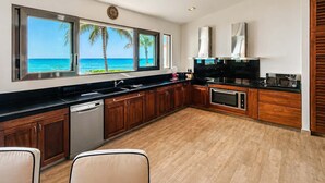 A modern kitchen with a view of the ocean, wooden cabinets, and a black countertop. - Beachfront 5BR Villa Playacar, Private Pool (Playa del Carmen)
