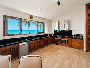 Eine moderne Küche mit Meerblick, Holzschränken und einer schwarzen Arbeitsplatte.