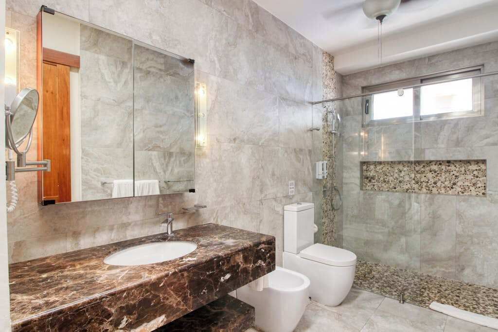 A bathroom with a marble sink, a toilet, and a glass-enclosed shower.