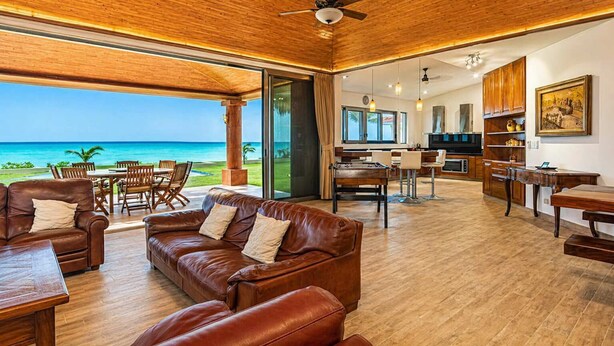 A spacious living area with a leather sofa, wooden flooring, a dining table, and a kitchen area. - Beachfront 5BR Villa Playacar, Private Pool (Playa del Carmen)