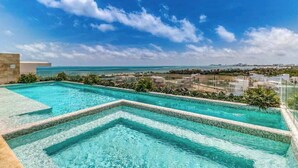 Une piscine à débordement située sur le toit, avec une eau d’un bleu cristallin, entourée de verdure et offrant une vue panoramique sur le paysage urbain côtier.