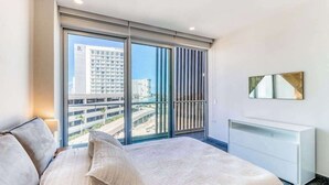 Une chambre d’hôtel moderne avec une grande fenêtre, un lit, une commode blanche et une vue sur la ville.