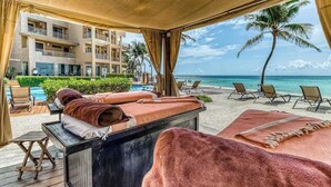 Area spa in spiaggia, con lettino da massaggio, asciugamani e poltrone relax.