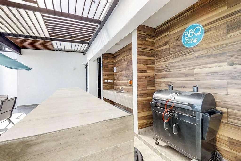 A modern outdoor area with a BBQ grill, a concrete seating area, and a wooden wall with a BBQ Zone sign.