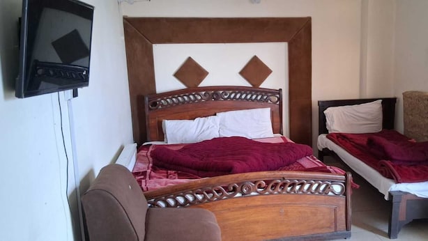 Una habitación de hotel con una cama de madera, una cama más pequeña, un televisor y una silla.