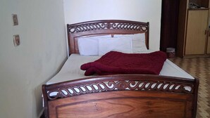 Una cama individual con cabecera de madera, ropa de cama blanca y una colcha roja.