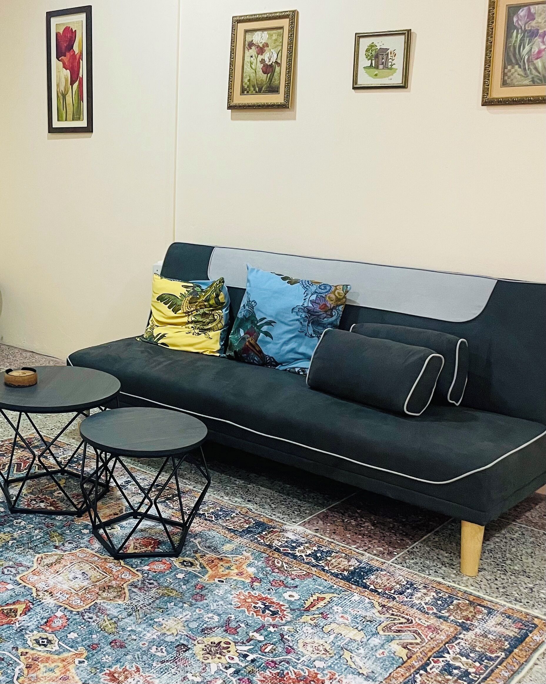 A black sofa with patterned cushions, a small round table, and a colorful rug.